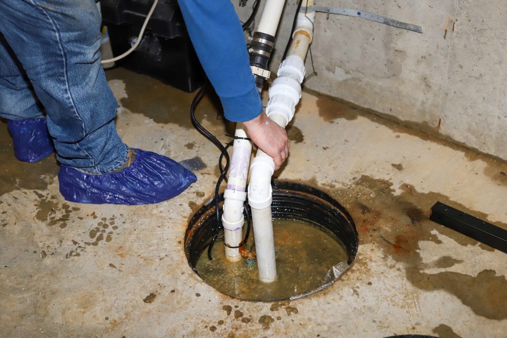 A plumber repairing a sump pump in a flooded basement
